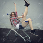 Happy beautiful teen girl driving shopping cart outdoor, image toned and noise added.